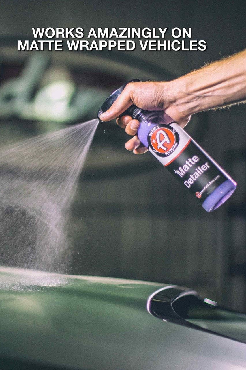 Hand spraying detailing product onto a dark green car hood.