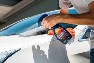 Person polishing a white car with a blue spray bottle and cloth