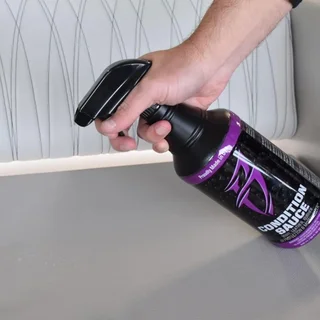 Hand holding a black spray bottle of all-purpose cleaner by a gray table.