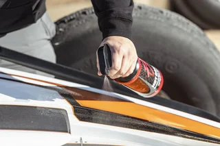 Hand using a spray can on a white and orange vehicle beside a tire