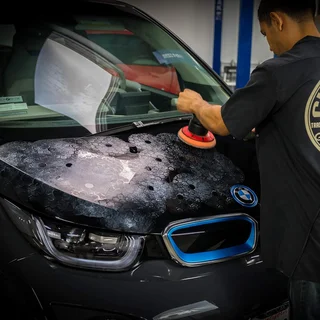 Man polishing the hood of a black BMW in a garage.