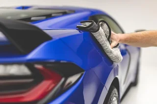 Hand drying the side mirror of a blue sports car.