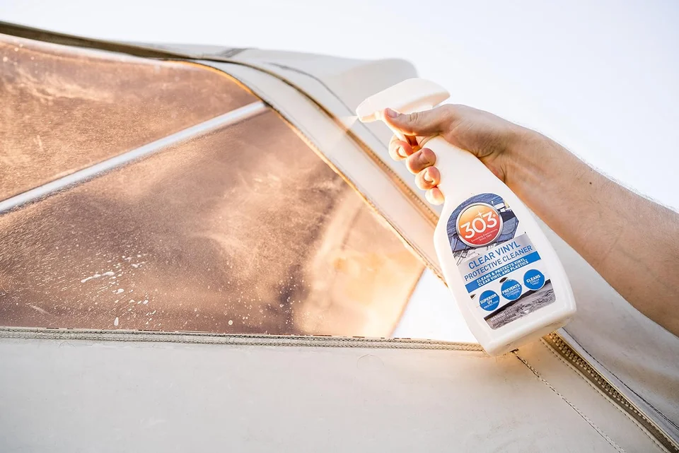 Hand holding spray cleaner against a dusty car windshield in sunlight