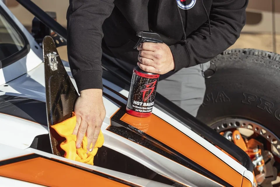 Person wiping orange and white sports car with a yellow cloth.