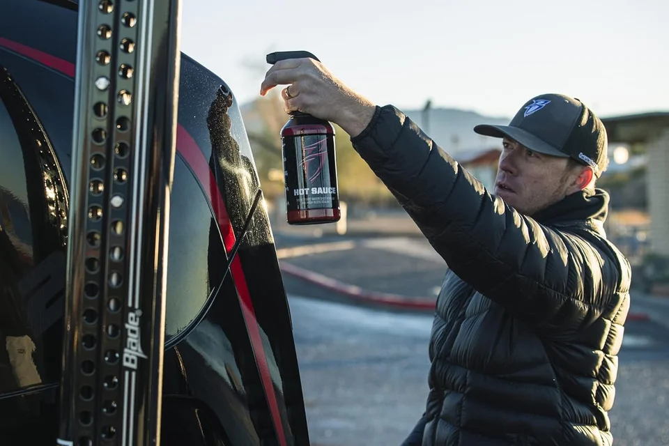 Man in a black puffer jacket hangs a lantern on an off-road vehicle at dusk.