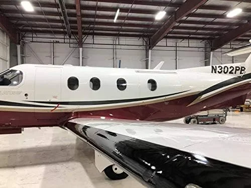 Private jet parked inside a hangar, white with maroon and gold stripes.