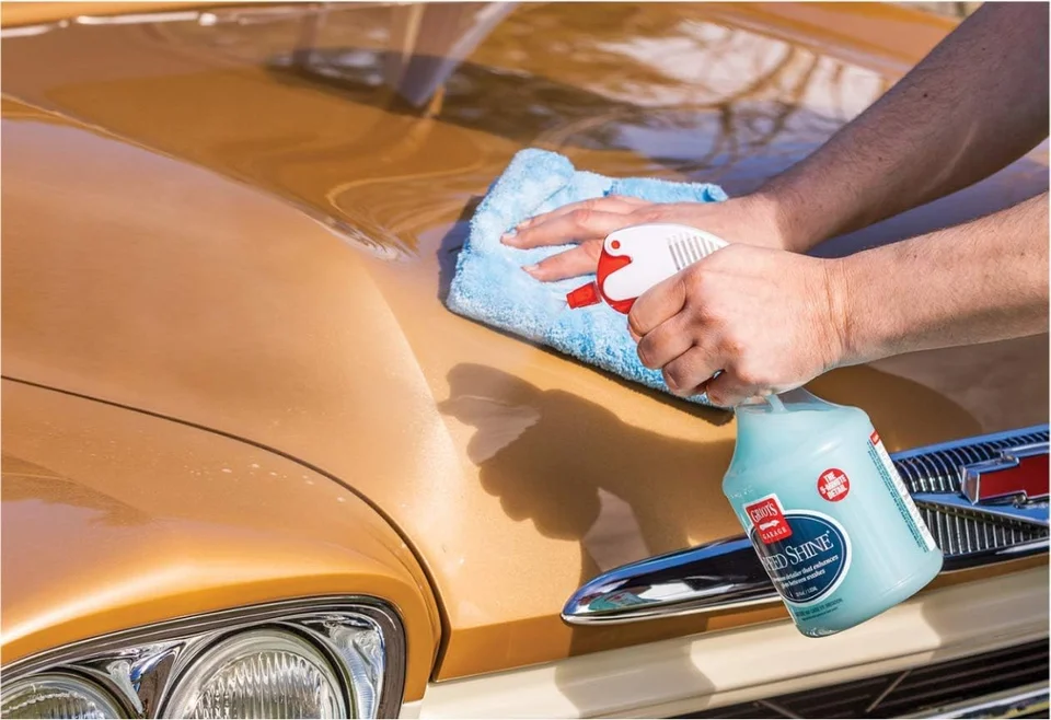 Hand cleaning the hood of a gold vintage car with a blue cloth and cleaner