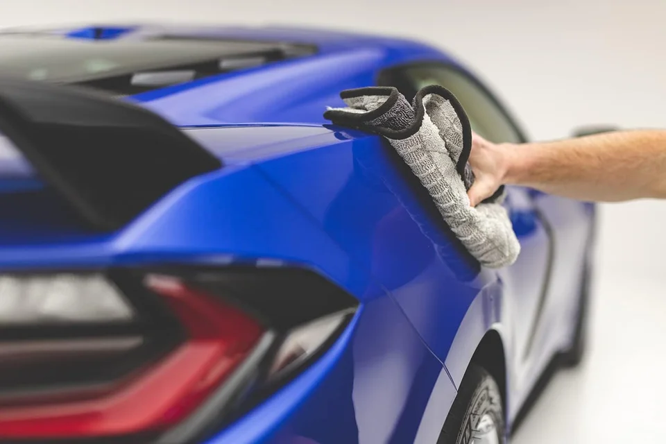 Hand drying the side mirror of a blue sports car.