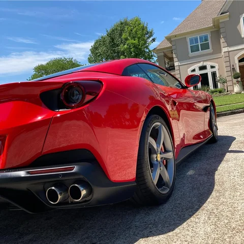 Red sports car parked in a suburban driveway, rear view in bright sunlight