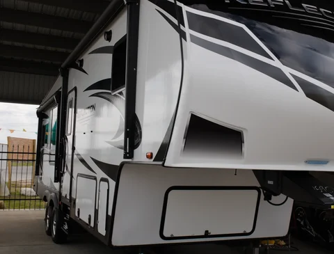 White fifth-wheel RV trailer parked under a roofed area.