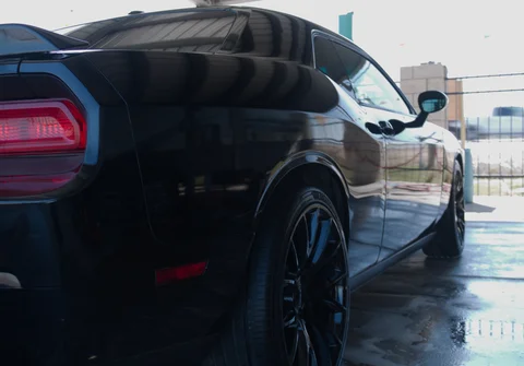 Black sports car parked on wet pavement, rear side view.